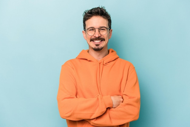 Young caucasian man isolated on blue background who feels confident crossing arms with determination