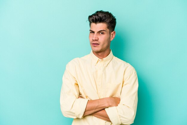 Young caucasian man isolated on blue background who is bored, fatigued and need a relax day.