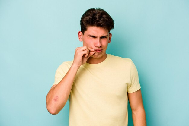 Young caucasian man isolated on blue background with fingers on lips keeping a secret