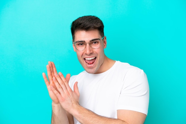 Young caucasian man isolated on blue background With glasses and applauding