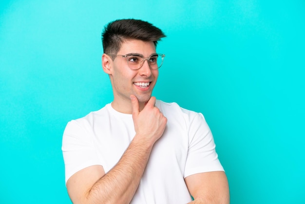 Young caucasian man isolated on blue background With glasses and thinking while looking up