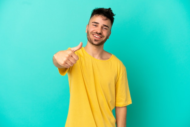 Young caucasian man isolated on blue background with thumbs up because something good has happened