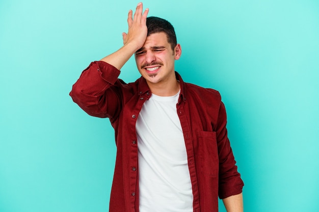 Young caucasian man isolated on blue forgetting something, slapping forehead with palm and closing eyes.