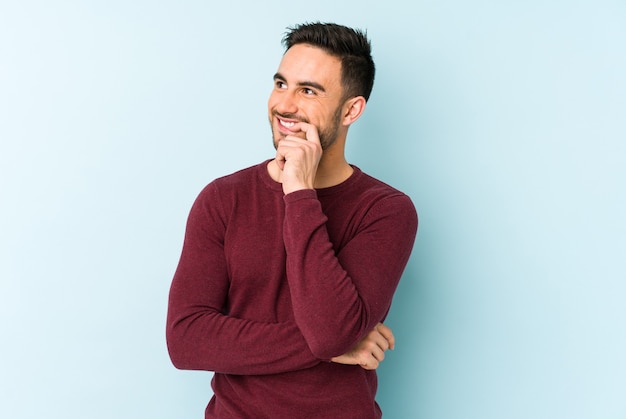 Young caucasian man isolated on blue relaxed thinking about something looking at a copy space.