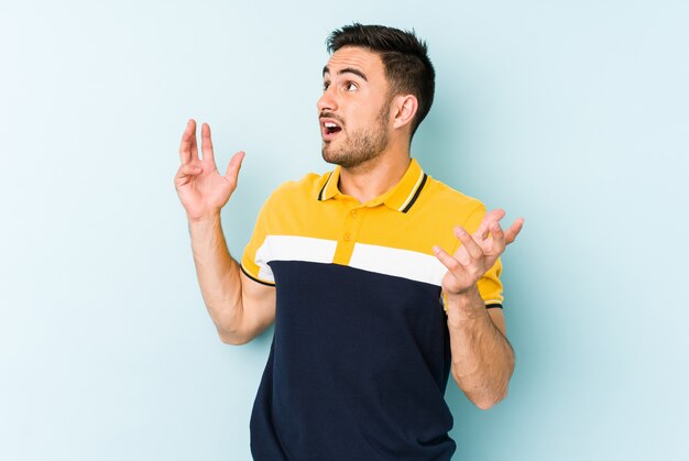 Young caucasian man isolated on blue screaming to the sky, looking up, frustrated.