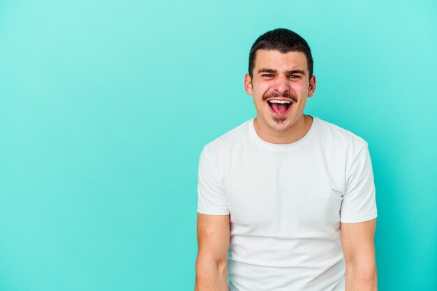 Young caucasian man isolated on blue shouting very angry, rage concept, frustrated.