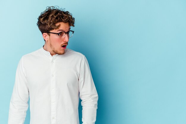 Young caucasian man isolated on blue wall being shocked because of something she has seen.