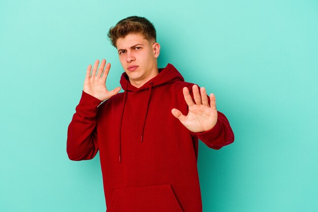 Young caucasian man isolated on blue wall being shocked due to an imminent danger