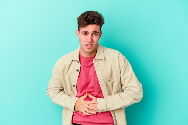 Young caucasian man isolated on blue wall having a liver pain, stomach ache.