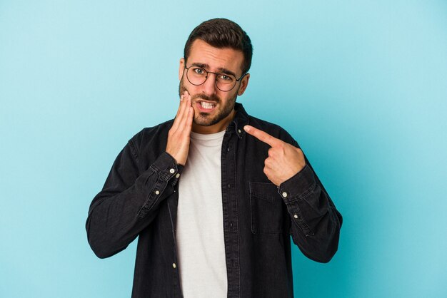 Young caucasian man isolated on blue wall having a strong teeth pain, molar ache.