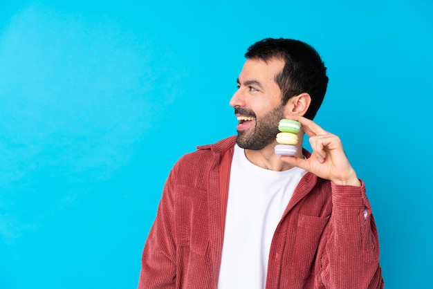 Young caucasian man over isolated blue wall holding colorful French macarons and thinking an idea