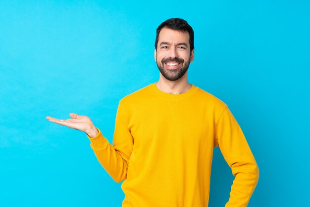 Young caucasian man over isolated blue wall holding copyspace imaginary on the palm to insert an ad