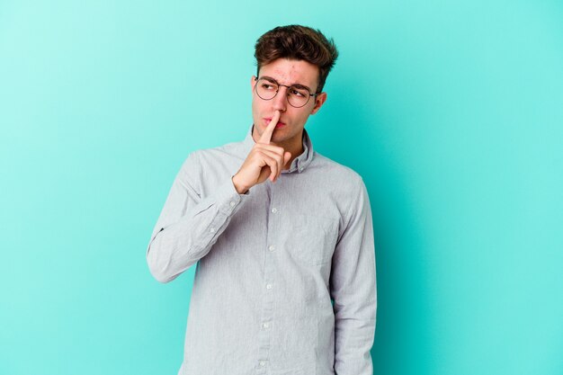 Young caucasian man isolated on blue wall keeping a secret or asking for silence