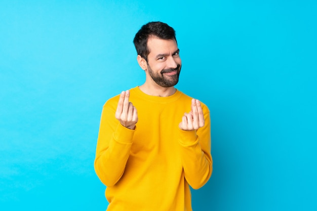 Young caucasian man over isolated blue wall making money gesture