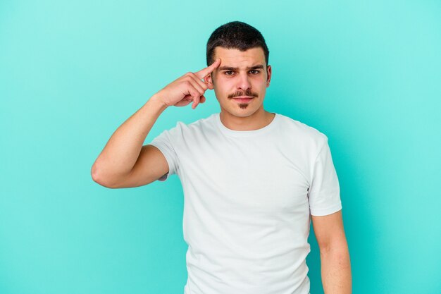 Young caucasian man isolated on blue wall pointing temple with finger, thinking, focused on a task.