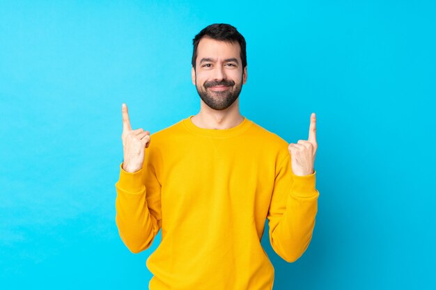 Young caucasian man over isolated blue wall pointing up a great idea