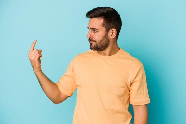 Young caucasian man isolated on blue wall pointing with finger at you as if inviting come closer.