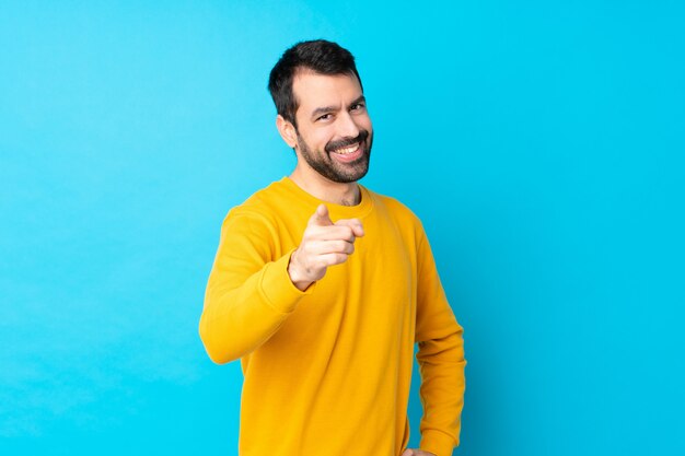 Il giovane uomo caucasico sopra la parete blu isolata indica il dito con un'espressione sicura