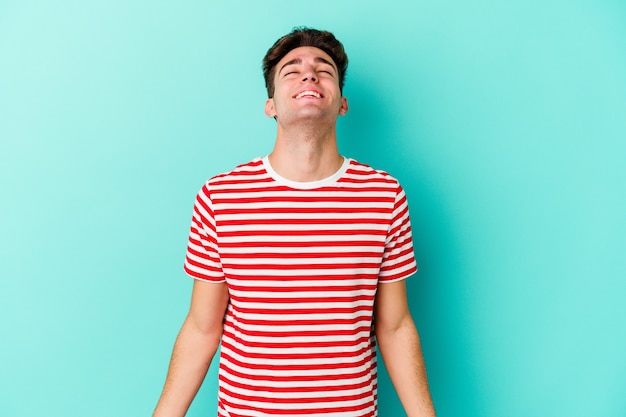 Young caucasian man isolated on blue wall relaxed and happy laughing, neck stretched showing teeth.