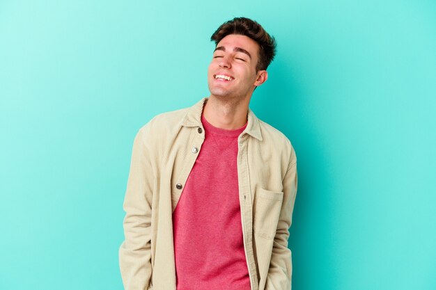 Young caucasian man isolated on blue wall relaxed and happy laughing, neck stretched showing teeth.