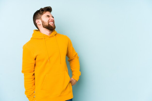 Young caucasian man isolated on blue wall relaxed and happy laughing, neck stretched showing teeth.