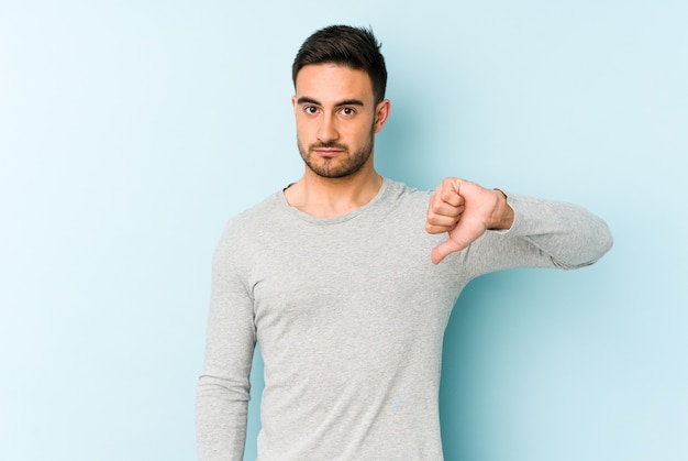 Young caucasian man isolated on blue wall showing a dislike gesture, thumbs down. Disagreement concept.