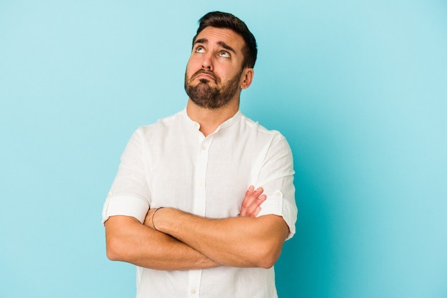 young caucasian man isolated on blue wall tired of a repetitive task