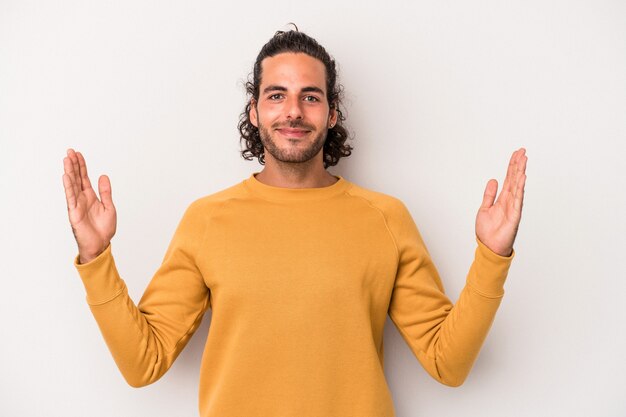 Young caucasian man isolated on gray background holding something little with forefingers, smiling and confident.