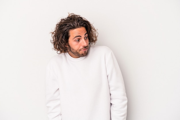 Young caucasian man isolated on gray background shrugs shoulders and open eyes confused.