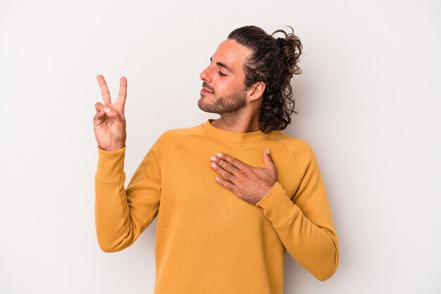 Young caucasian man isolated on gray background taking an oath, putting hand on chest.