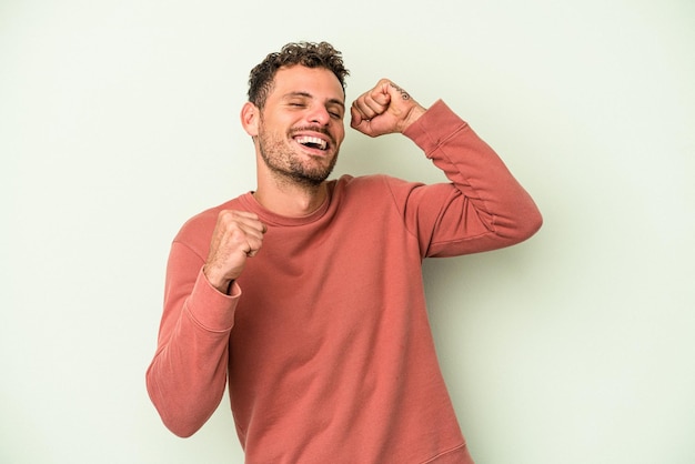 Young caucasian man isolated on green background celebrating a special day, jumps and raise arms with energy.