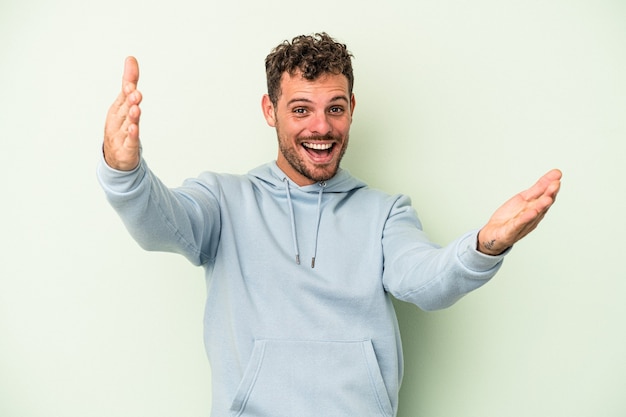 Giovane uomo caucasico isolato su sfondo verde che celebra una vittoria o un successo, è sorpreso e scioccato.