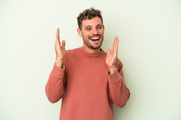 Il giovane uomo caucasico isolato su sfondo verde ride forte tenendo la mano sul petto.