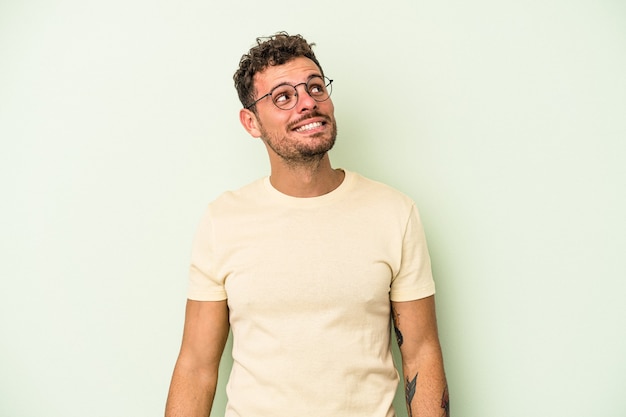 Young caucasian man isolated on green background relaxed and happy laughing, neck stretched showing teeth.