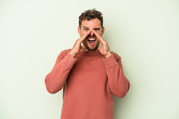 Young caucasian man isolated on green background saying a gossip, pointing to side reporting something.