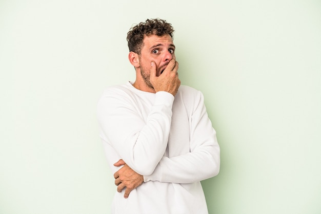 Young caucasian man isolated on green background scared and afraid.