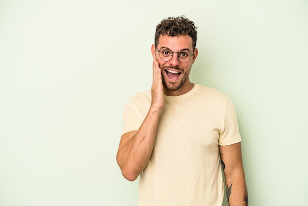 Young caucasian man isolated on green background shouts loud, keeps eyes opened and hands tense.