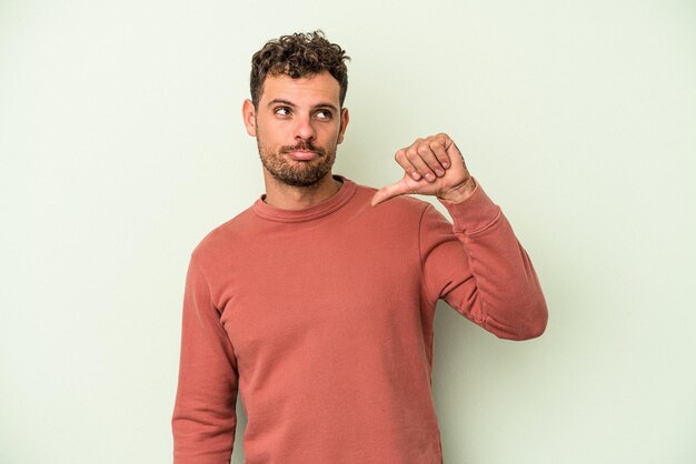 Young caucasian man isolated on green background showing a dislike gesture, thumbs down. Disagreement concept.