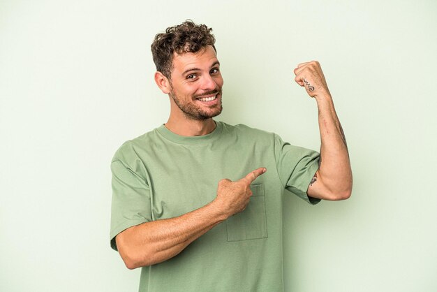 Young caucasian man isolated on green background showing strength gesture with arms, symbol of feminine power