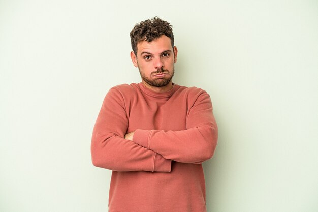 Young caucasian man isolated on green background shrugs shoulders and open eyes confused.