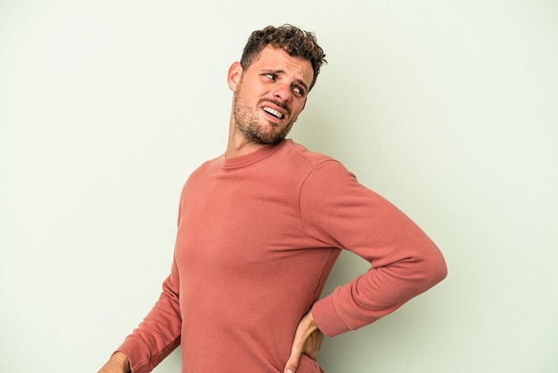 Young caucasian man isolated on green background suffering a back pain.