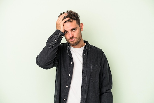 Young caucasian man isolated on green background tired and very sleepy keeping hand on head.