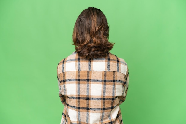 Young caucasian man isolated on green chroma background in back position