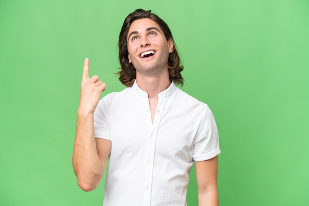 Young caucasian man isolated on green chroma background pointing up and surprised