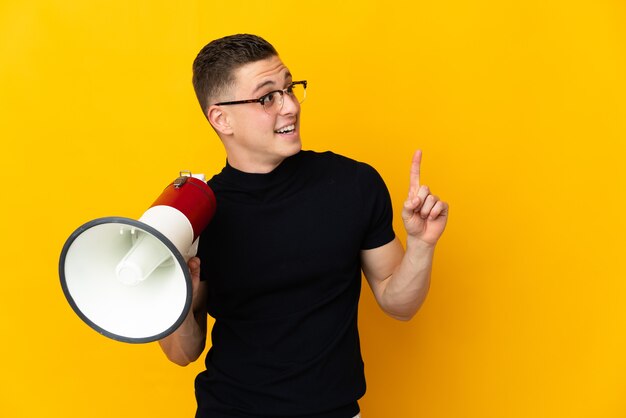 Young caucasian man isolated holding a megaphone and intending to realizes the solution