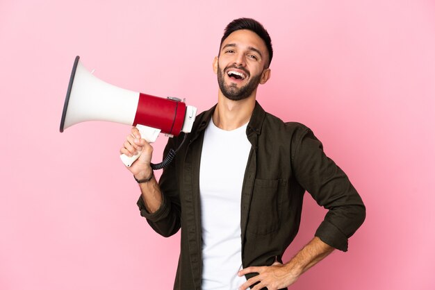 Young caucasian man isolated holding a megaphone and smiling