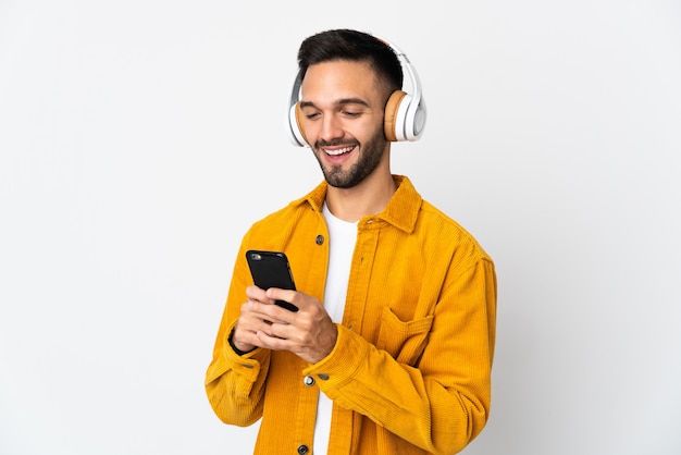 Young caucasian man isolated listening music and looking to mobile