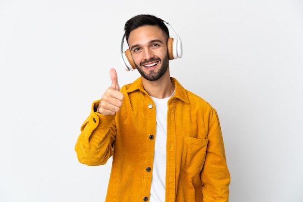 Young caucasian man isolated listening music and with thumb up