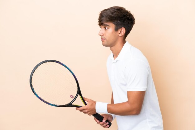 Young caucasian man isolated on ocher background playing tennis