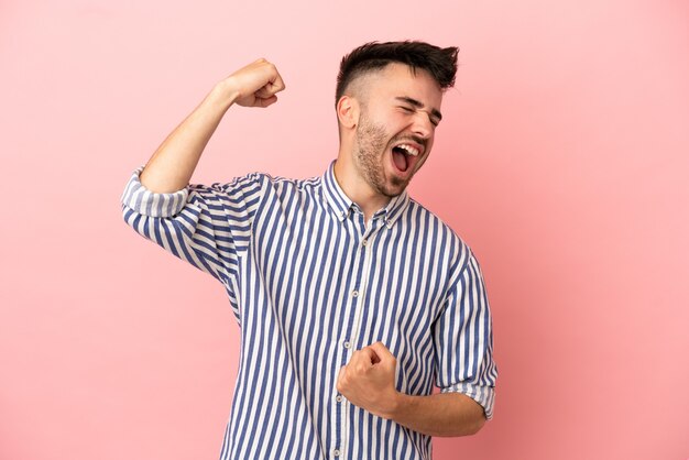 勝利を祝うピンクの背景に孤立した若い白人男性